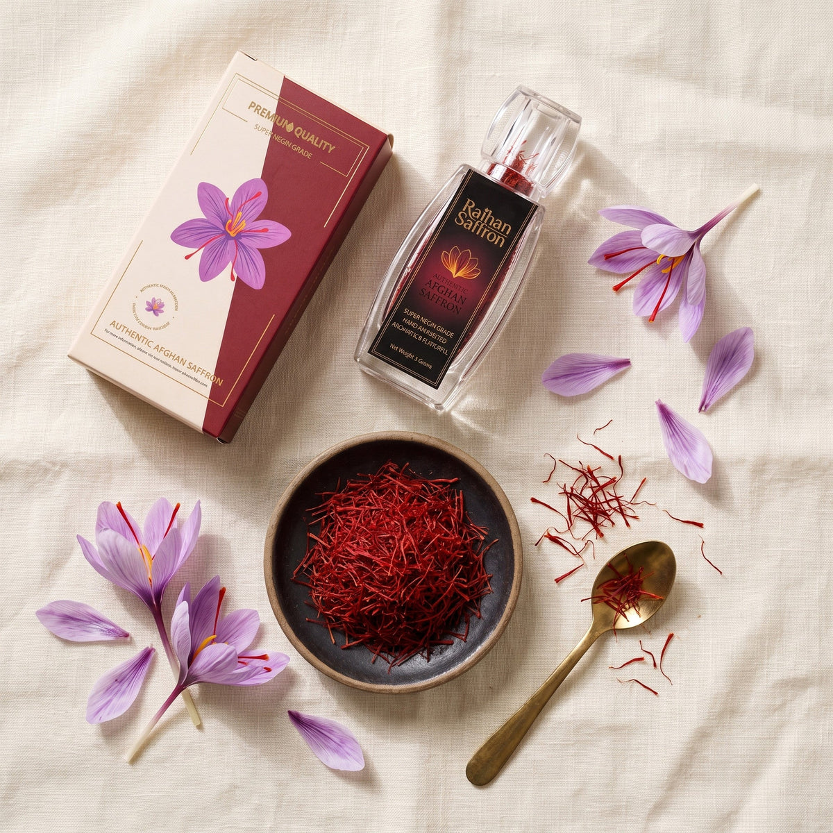 Overhead flat-lay of Raihan saffron box, bottle, saffron threads, brass spoon and crocus flowers on linen