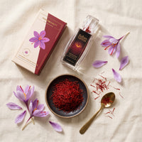 Overhead flat-lay of Raihan saffron box, bottle, saffron threads, brass spoon and crocus flowers on linen